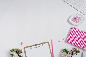 Home office desk workspace with blank paper clipboard, notepad, keyboard, stationery and apple tree flowers on white background with copy space. Flat layout, top view photo