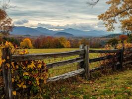 A Rustic Wooden Fence Frames a Distant Mountain Range Under a Cloudy Sky with Autumnal Foliage photo