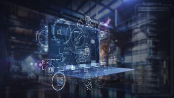 The laptop displays a futuristic control interface against a factory backdrop video