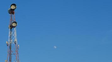 telecommunications tower stands against clear blue sky with moon visible. photo