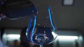 Bartender in a nightclub, working behind the counter in neon blue light, adds an excessive amount of ice cubes to a glass. Bottom view video