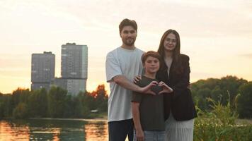 Portrait of family consisting of three members. father, mother, and child. All three are looking directly at camera, smiling warmly, and forming heart shape with their hands. video