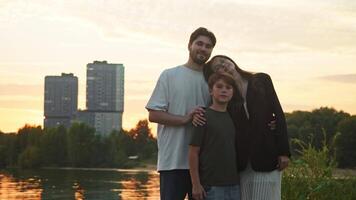 Portrait of a happy family of three, consisting of a mother, father, and child, is shown standing in a city park. In background, a newly constructed high-rise apartment building is visible, in which family has purchased an apartment. video