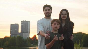 Young father, mother, and their son are seen looking directly into the camera. They are smiling warmly and making a gesture that represents a heart. video