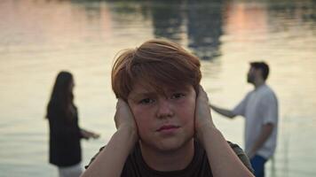Portrait of a frustrated and depressed boy whose parents are loudly and actively swearing in the background video
