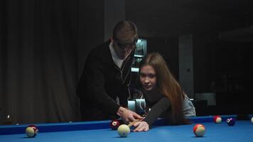 a young man teaches his girlfriend to play billiards. He explains the rules of the American pool game and guides her cue video