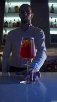 Bartender stands at the bar and pushes the Spritz Aperol cocktail directly towards the camera. Close up. Slow motion. Vertical video