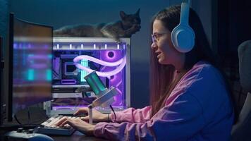 Young woman is playing an online first-person shooter game on a computer, using a mouse and keyboard, in evening, under a neon pink and turquoise lighting. video