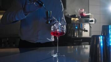 A bartender at a nightclub pours whiskey with a mixer into a glass filled with ice that sparkles in the neon light., video