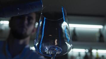 Bartender at a nightclub adds a significant number of ice cubes are added to an empty cocktail glass, which is illuminated by blue neon lighting, at the bar counter. video