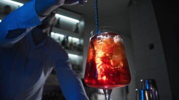 Bartender at the bar prepares a refreshing orange cocktail, a red cocktail with ice cubes and skillfully mixes it with a bar spoon. Close up. Slow motion video