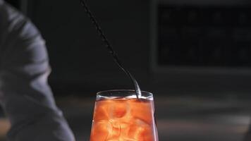 Close-up of the creation of a refreshing orange cocktail aperol spritz with ice, which the bartender stirs with a bar spoon. Close up. Slow motion video