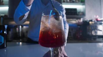 Bartender in the nightclub, standing behind the bar, prepares a cocktail by stirring a spoon in a glass filled with ice, resulting in a delightful Aperol Spritz with a subtle orange flavor. video