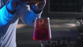 Bartender in nightclub prepares beverage, infusing it with essence of orange by vigorously pressing and twisting peel, before adding it to cocktail. video