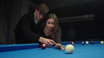 Young man teaches his beloved to play billiards. He talks in detail about rules of the American pool and helps her hold cue. In process of learning, he gently hugs her. video