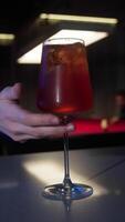 Close-up of serving a cold refreshing orange alcoholic cocktail on the bar counter to a customer from a bartender against the background of a game of billiards video