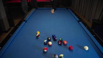 An American pool player smashes multicolored balls lying in shape of pyramid on blue billiard table with well-aimed and strong blow video