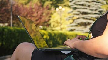 Close-up shot of a woman's hands is shown, sitting on a park bench during summer months. She is holding a laptop computer on her lap and is typing enthusiastically on the device, while it is outside. video