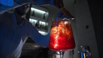 Barman in nightclub prepares drink, he incorporates the essence of orange by vigorously squeezing and twisting peel, then adding it to cocktail. video