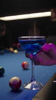 Young woman is holding a bright blue cocktail in her hand, against a backdrop of a pool table. Friends are playing American pool in a bar. video