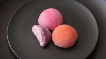 Delicious colorful asian mochi sweets with rice dough shell and fruit filling on dark concrete background video