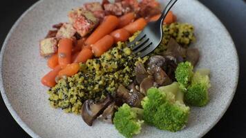 Colorful vegan vegetarian dish consists of tofu, broccoli, quinoa, mushrooms and carrots on a dark textured background video
