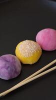 Delicious colorful asian mochi sweets with rice dough shell and fruit filling on dark concrete background video