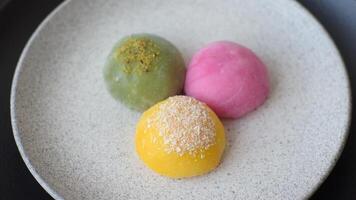 Delicious colorful asian mochi sweets with rice dough shell and fruit filling on dark concrete background video