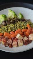 Colorful vegan vegetarian dish consists of tofu, broccoli, quinoa, mushrooms and carrots on a dark textured background video