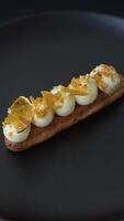 Sweet dessert eclairs or profiteroles with chocolate filling and covered with cream and dried oranges on a dark concrete background video