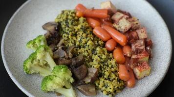 Colorful vegan vegetarian dish consists of tofu, broccoli, quinoa, mushrooms and carrots on a dark textured background video