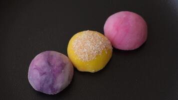 Delicious colorful asian mochi sweets with rice dough shell and fruit filling on dark concrete background video