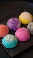 Delicious colorful asian mochi sweets with rice dough shell and fruit filling on dark concrete background video