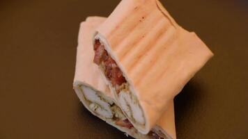 Roll with pita, meat, tomatoes, cheese, sauce, salt and spices on a dark texture background video