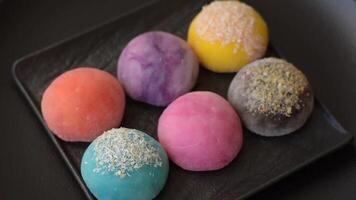 Delicious colorful asian mochi sweets with rice dough shell and fruit filling on dark concrete background video