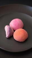 Delicious colorful asian mochi sweets with rice dough shell and fruit filling on dark concrete background video