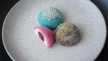 Delicious colorful asian mochi sweets with rice dough shell and fruit filling on dark concrete background video