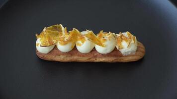 Sweet dessert eclairs or profiteroles with chocolate filling and covered with cream and dried oranges on a dark concrete background video