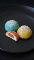 Delicious colorful asian mochi sweets with rice dough shell and fruit filling on dark concrete background video