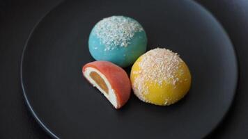 Delicious colorful asian mochi sweets with rice dough shell and fruit filling on dark concrete background video