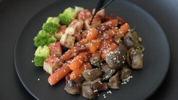 Colorful vegan vegetarian dish consists of tofu, broccoli, quinoa, mushrooms and carrots on a dark textured background video