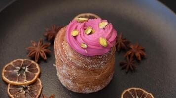 Sweet craffin or panettone garnished with raspberry and pistachio flavored cream on a dark concrete background video