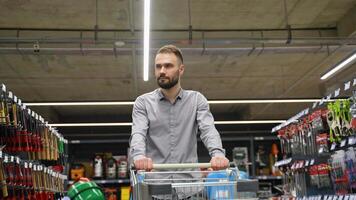 A man walking with trolley in a hardware store chooses a new axe video
