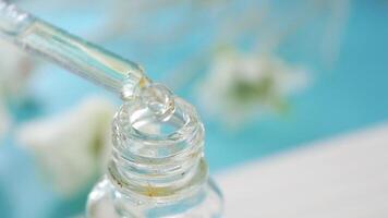 A closeup photograph of a dropper bottle filled with serum resting on a soft background video