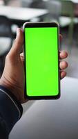 A hand holds a smartphone showing a bright green screen, ideal for customization video