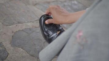An individual is adjusting their stylish black shoe while sitting on a cobblestone path video