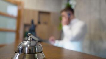 Front desk bell for call staff service. Friendly receptionist talking on phone at counter in hotel video