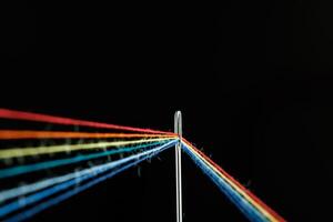 multi-colored threads for sewing in the form of a rainbow pass through an antique needle on a black background photo