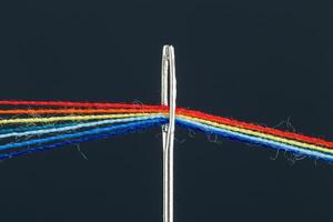 multi-colored threads for sewing in the form of a rainbow pass through an antique needle on a black background photo