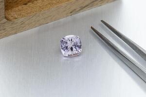 macro mineral faceted stone Morganite with tweezers on a gray background photo